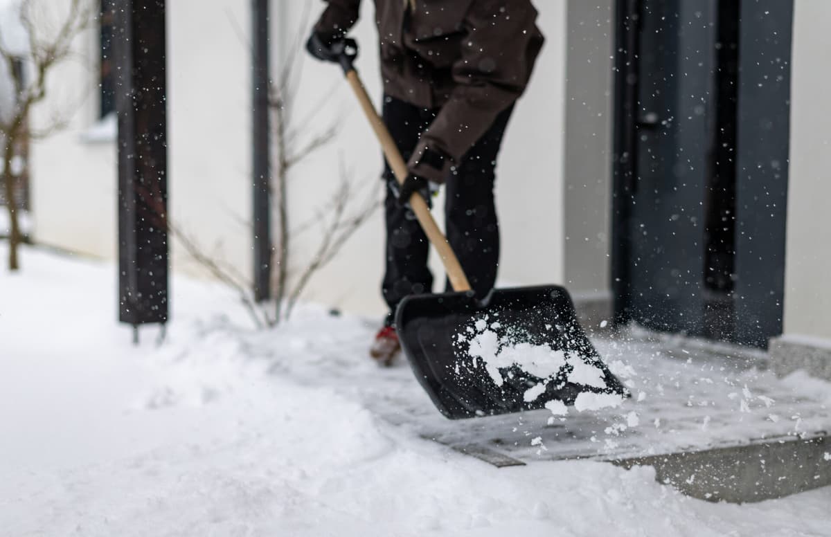 Close-up of a snow shovel being used to clear snow from the front door of a house