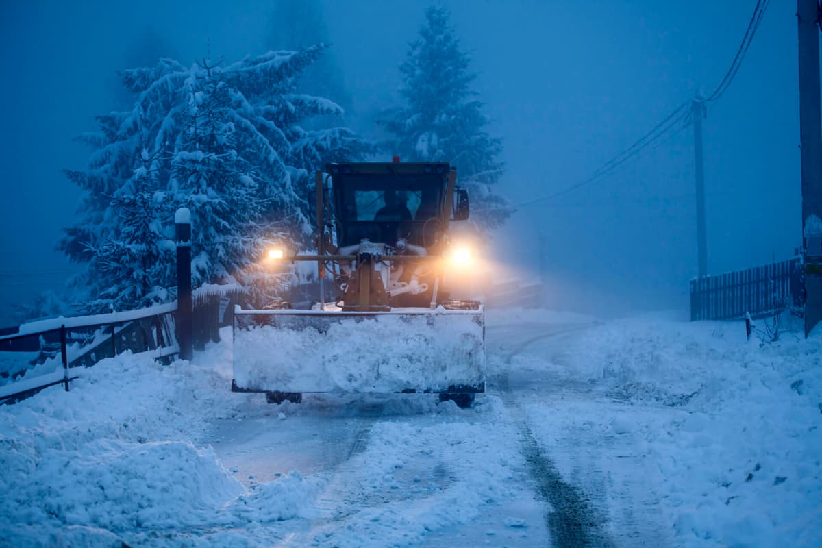 A snow plow clearing a road in winter, early morning
