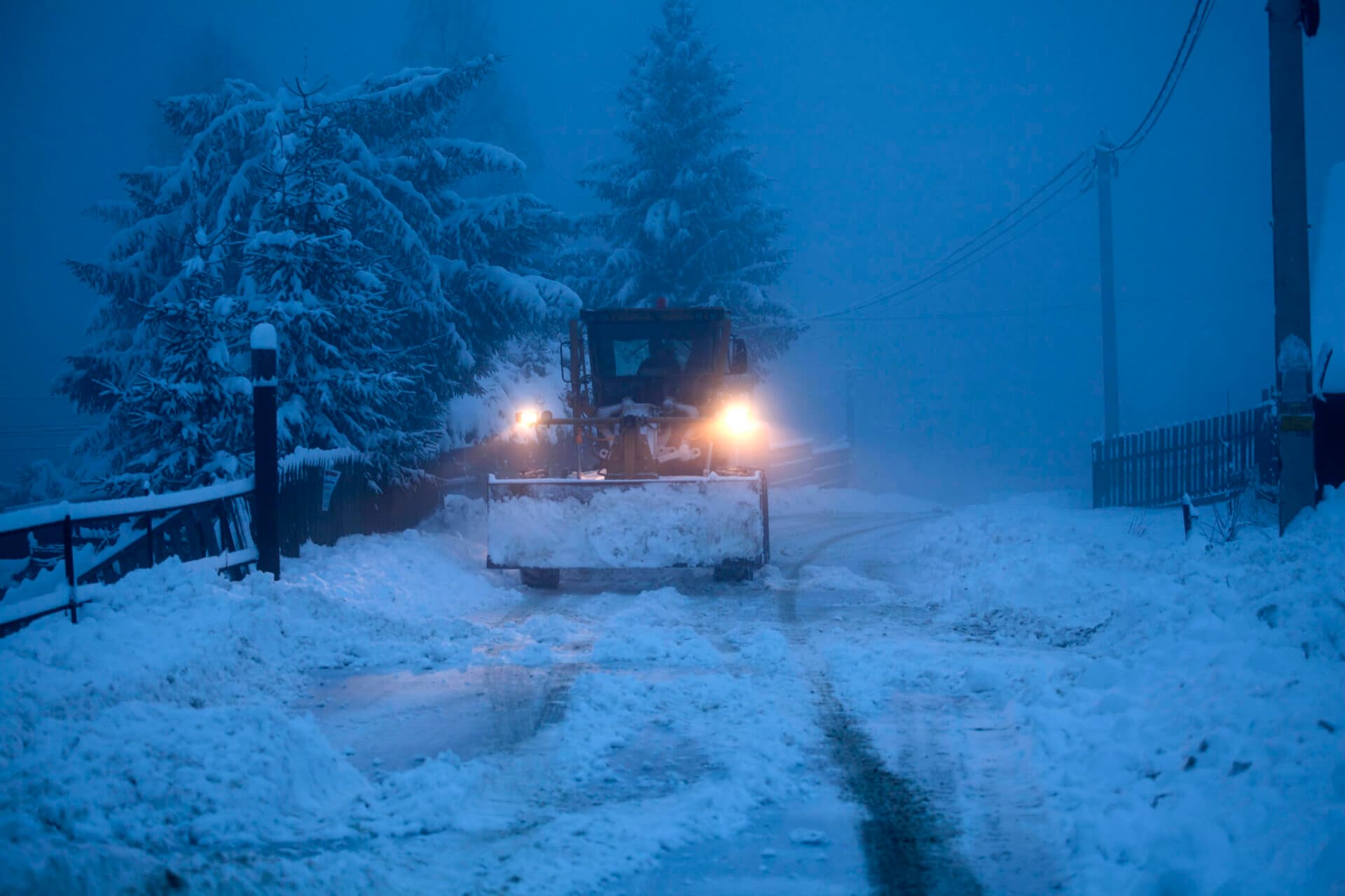 A snow plow clearing a road in winter, early morning